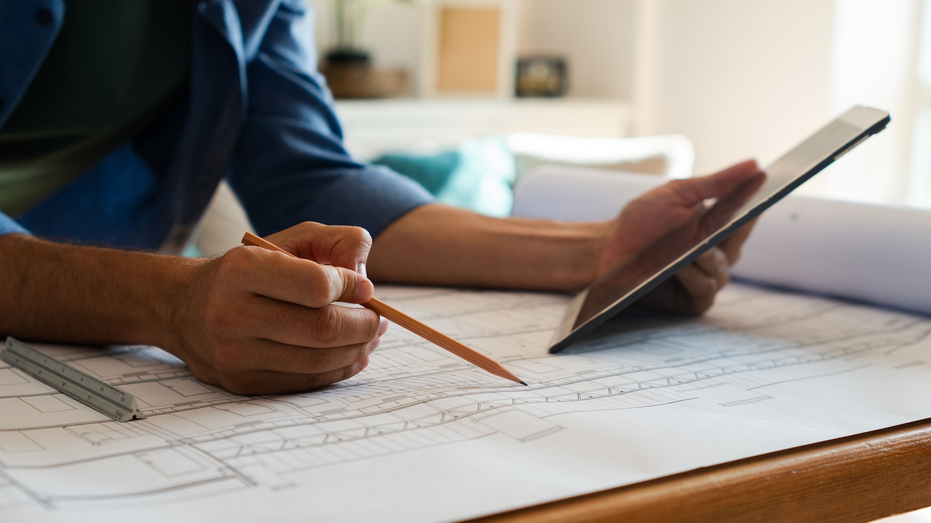 Architect using digital tablet and pencil on blueprint in home office